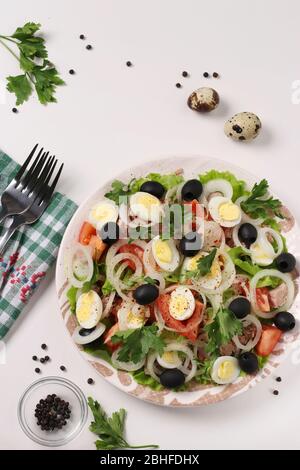 Salade saine avec thon en conserve, tomates, œufs de caille, olives noires, oignons blancs et laitue biologique sur fond blanc, vue de dessus Banque D'Images