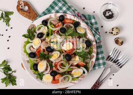 Salade saine avec thon en conserve, tomates, œufs de caille, olives noires, oignons blancs et laitue biologique sur fond blanc, vue de dessus Banque D'Images