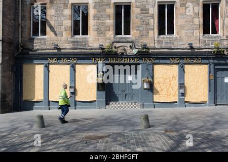 C'est le verrouillage du Coronavirus. Un ouvrier solitaire passe devant un pub embarqué dans le Grassmarket d'Édimbourg. Banque D'Images