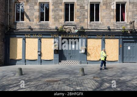 C'est le verrouillage du Coronavirus. Un ouvrier solitaire passe devant un pub embarqué dans le Grassmarket d'Édimbourg. Banque D'Images