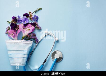 Fleurs avec masque et stéthoscope sur fond bleu. Concept de bonne journée d'infirmière. Vue de dessus Banque D'Images