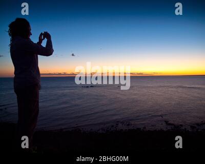 Fille prend une photo smartphone du lever du soleil au-dessus de l'océan Indien, Pender Bay, Dampier Peninsula, Australie occidentale Banque D'Images