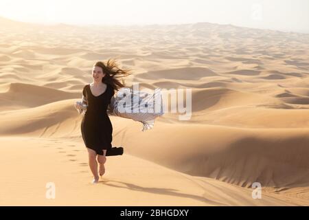 Une fille en robe noire est tombée dans une tempête de sable entre les dunes et les montagnes. Banque D'Images