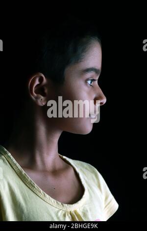 Portrait d'une petite fille indienne avec des cheveux courts. Bel œil d'un enfant sur fond noir. Un look dramatique d'une petite fille en Inde. Banque D'Images