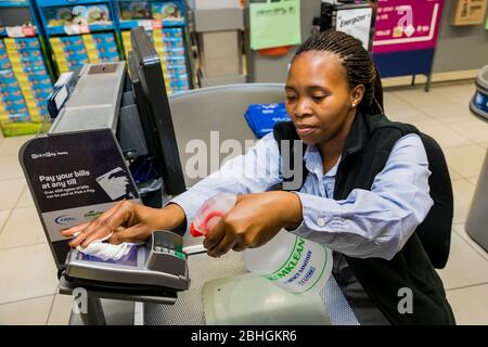 Cape Town, Afrique du Sud - 23 mars 2020: Le personnel du caissier de caisse a nettoyé la machine à cartes de crédit à l'épicerie Pick 'n Pay pendant l'épidémie de virus Banque D'Images