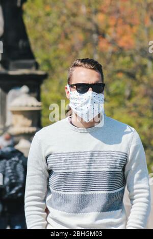 Jeune homme avec lunettes de soleil et masque en tissu cousu photographié sur le pont Charles à Prague, en République tchèque. Arrière-plan flou. Voyager, tourisme pendant coronavirus. COVID-19. Photo verticale. Banque D'Images