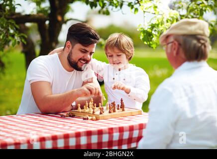 famille heureuse de trois générations d'hommes jouant aux échecs dans le jardin de printemps Banque D'Images