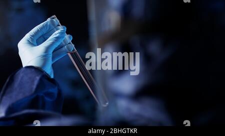 Assistant de laboratoire en combinaison protectrice pour étudier l'échantillon dans une cuvette en tube de verre de laboratoire. Gros plan sur la mise au point sélective. Banque D'Images