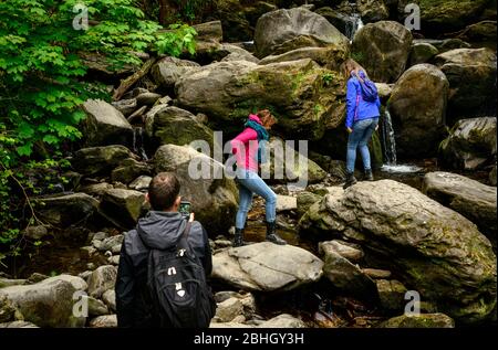 Groupe mixte de touristes sur des rochers à Torc Waterfall dans le parc national de Killarney, comté de Kerry, Irlande Banque D'Images