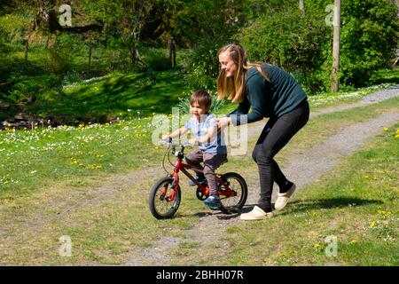 Mère jouant avec son jeune garçon de 3 ans l'aidant à apprendre à faire du vélo pendant le maintien dans Carmarthenshire Pays de Galles Royaume-Uni KATHY DEWITT Banque D'Images