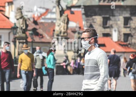 Jeune homme avec lunettes de soleil et masque en tissu cousu photographié sur le pont Charles à Prague, en République tchèque. Brouillé dans l'arrière-plan. Voyager, tourisme pendant coronavirus. COVID-19. Banque D'Images