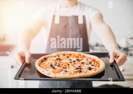 Gros plan de pizza italienne fraîche chaude margherita avec des olives dans les mains du chef mâle Banque D'Images