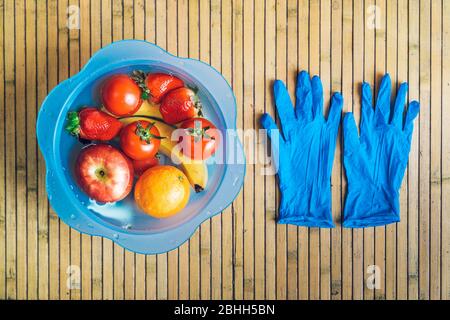 Bol bleu avec différents fruits frais et propres sur une base en bois avec des gants en latex bleu. Bananes, tomates, pommes, fraises et oranges immergées Banque D'Images