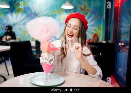 France doux dessert national, fille en béret rouge mange gâteau rose, bonbons floss et milkshake, rire et sourires Banque D'Images