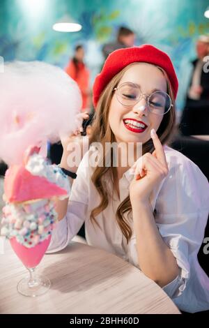 Dessert sucré avec bonbons en coton rose, milkshake et gâteau. Fille en béret rouge et verres, café en France Banque D'Images