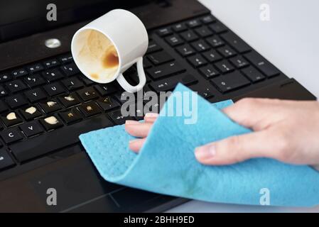 La main nettoie le café renversé sur le clavier de l'ordinateur portable avec un chiffon Banque D'Images