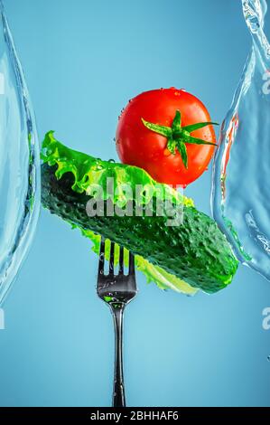 concombre, tomate et laitue sur une fourchette dans des éclaboussures d'eau sur fond bleu. légumes, nature, frais, saine, alimentation brute Banque D'Images