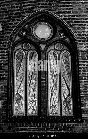 Ancienne fenêtre en arc sur un mur de briques en couleur monochrome. Un détail de proximité d'une église. Banque D'Images