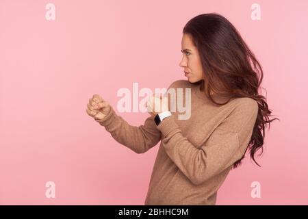 Battons-nous ! Vue latérale d'une jeune femme confiante avec des cheveux ondulés brunette tenant les poings prêts à poinçonner, boxe avec une expression déterminée agressive. Banque D'Images