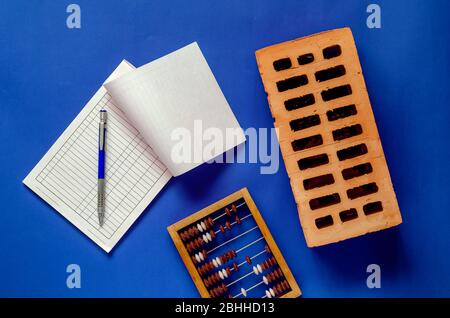 Brique, facture vierge et abacus en bois sur un fond bleu. Nouvelle brique rouge, facture vierge avec stylo et abacus en bois vissé. Sujets de construction Banque D'Images