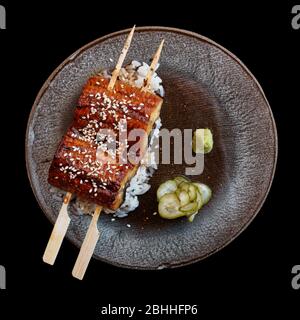 Anguille unagi frite avec sauce barbecue et riz tiré d'en haut isolé sur fond noir Banque D'Images