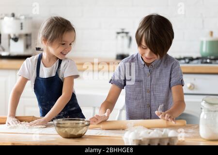 Enfants enfants en bas âge et frères et sœurs en train de jouer avec de la farine dans la cuisine. Banque D'Images