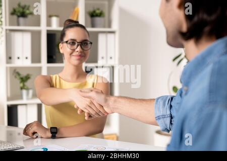 Vue sur l'épaule de l'homme faisant poignée de main avec une femme d'affaires attrayante après réunion au bureau, concept de partenariat de démarrage Banque D'Images