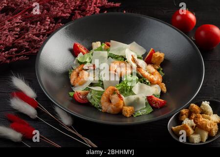 salade césar avec crevettes dans une plaque noire sur fond en bois sombre Banque D'Images