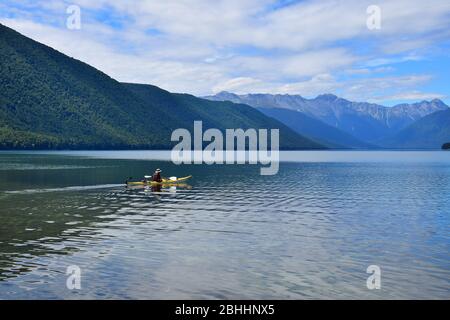 Un homme dans un canoë jaune pagayant à travers le lac Rotoroa. Montagnes en arrière-plan. Parc national des lacs Nelson, Tasman, Nouvelle-Zélande, île du Sud. Banque D'Images