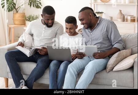 Famille masculine africaine avec ordinateur portable, tablette numérique et magazine à la maison Banque D'Images