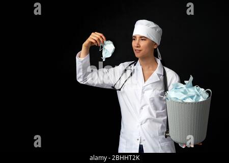 Le médecin tient un seau rempli de masques faciaux usagés, les jetant comme symbole de fin d'épidémie Banque D'Images