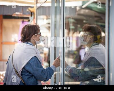 BELGRADE, SERBIE - 23 AVRIL 2020: La vieille femme âgée portant un masque respiratoire regardant sa réflexion dans un verre, pendant le covid du coronavirus Banque D'Images