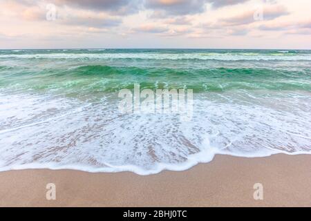 coucher de soleil nuageux au-dessus des eaux de la mer verte. vagues qui s'écrasent sur la plage de sable. horizon clair. temps vent changeant Banque D'Images