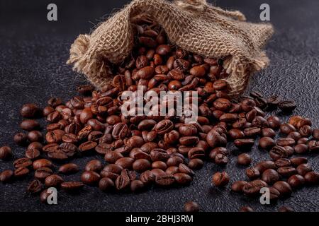 Grains de café aromatiques rôtis saupoudrés d'un sac en toile sur une surface sombre. Le concept de la tradition du café du matin. Vue latérale supérieure Banque D'Images