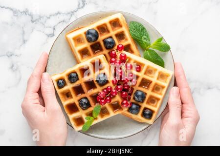 Assiette de gaufres belges avec baies et sirop dans les mains des femmes, vue de dessus. Délicieux petit déjeuner sucré Banque D'Images