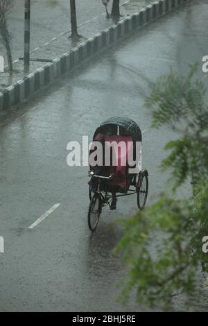 26 avril 2020 : lors de la pluie soudaine à midi, un arrache-pousse portant un masque facial et un imperméable transporte des passagers qui portent également un masque facial dans une rue vide à Dhaka, au Bangladesh; pendant la pandémie de coronavirus (Covid-19). Crédit: Shafayet Hossain Apollo/ZUMA Wire/Alay Live News Banque D'Images