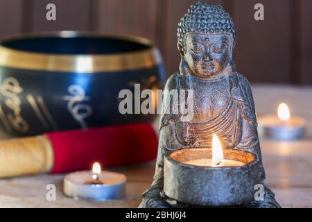 Bouddha assis en pierre, bougies et bol tibétain. Autour de la bougie, l'atmosphère de méditation. Confort et détente à la maison Banque D'Images