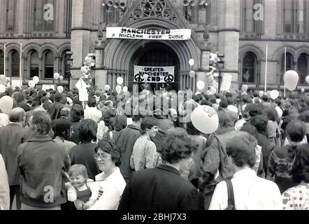 Les gens écoutent un orateur lors d'un rassemblement de campagne pour le désarmement nucléaire à Albert Square, à l'extérieur de l'hôtel de ville de Manchester, Grand Manchester, Angleterre, Royaume-Uni en 1983. Le Conseil municipal de Manchester a suspendu sa bannière « zone nucléaire libre de Manchester » au-dessus de l'entrée pour soutenir le pays. Banque D'Images