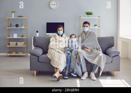 Famille malade dans les masques médicaux avec un plat assis sur un canapé regardant l'appareil photo avec de la fièvre à la maison attendant un médecin. Banque D'Images