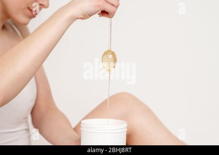 Femme tenant le bâton de miel tout en coulant la cire liquide dans le récipient sur fond blanc. Banque D'Images