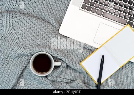 Plat de travail confortable de l'écriture avec le café chaud du sweat, l'ordinateur portable et les accessoires d'écriture. Travail de la maison. Écriture. Concept chaud par temps froid. Banque D'Images