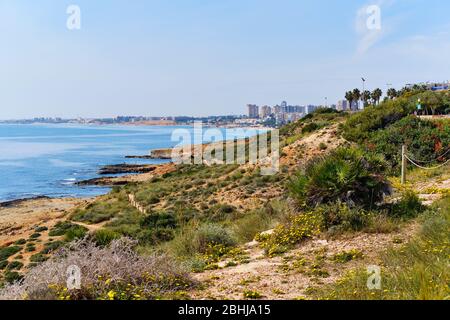 Dehesa de Campoamor haut bâtiment résidentiel ville, vue de la plage de Cabo Roig bord de mer rocheux. Mer Méditerranée bleue calme, journée ensoleillée, pas de personnes. Banque D'Images