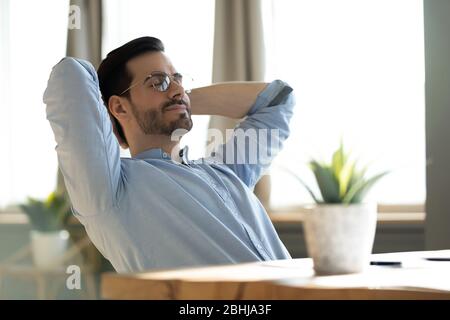 Un jeune homme paisible rêvant de jour, se penchant dans le dos, assis au bureau Banque D'Images