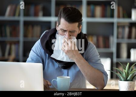 Homme d'affaires malade soufflant nez de course, assis au bureau Banque D'Images
