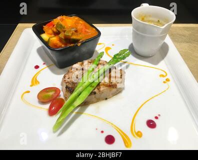 Photo de steak de porc avec morceaux de tomate et d'apparagus sur le plat blanc Banque D'Images