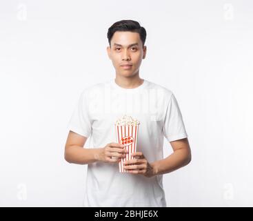 Jeune homme asiatique en t-shirt blanc tenant le popcorn et regardant la caméra isolée sur fond blanc. Banque D'Images