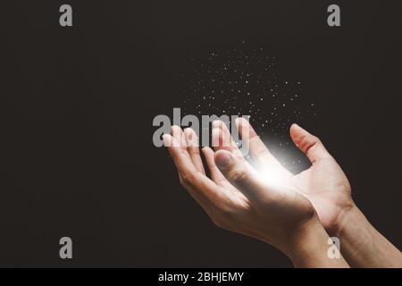 Mains mâles priant avec foi dans la religion pour la bénédiction de Dieu, les lumières croissantes et la poudre magique flottant sur les mains. Banque D'Images