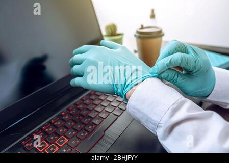 Une femme portant une paire de gants en caoutchouc à la menthe avant de travailler sur un ordinateur au bureau. Propreté et hygiène dans la lutte contre les virus Banque D'Images