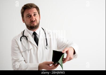 Portrait d'un médecin mâle avec stéthoscope en uniforme médical montrant un portefeuille vide posant sur un fond blanc isolé Banque D'Images