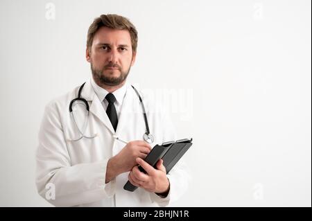 Portrait de belle femme médecin avec stéthoscope portant des gommages rouges, avec des cheveux bruns, prend des notes, regardant l'appareil photo se posant sur un blanc isolé Banque D'Images